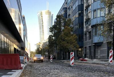 Brukowana ulica w Warszawie, z nowoczesnymi budynkami i wieżowcem Złota 44 w tle.