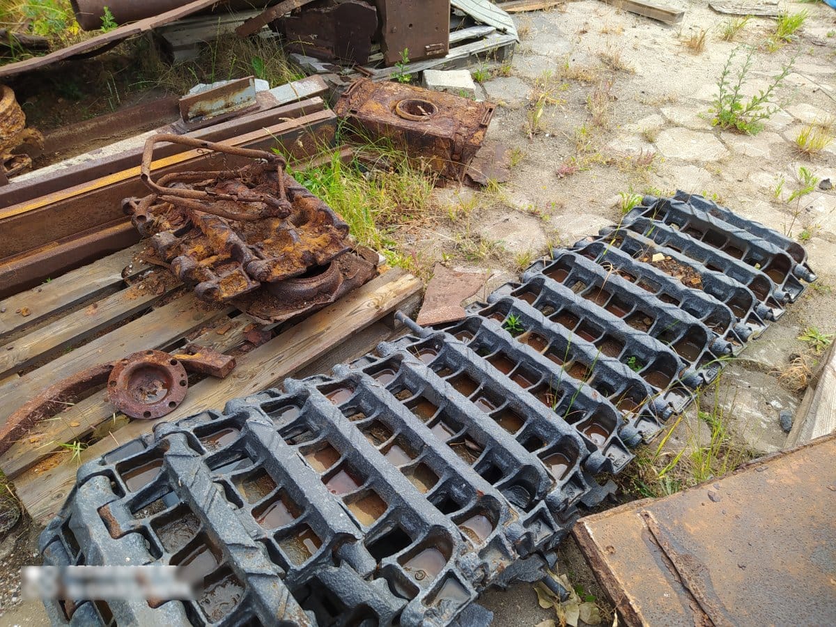Zardzewiałe części koparki i elementy gąsienic leżą na drewnianej palecie na zewnątrz.