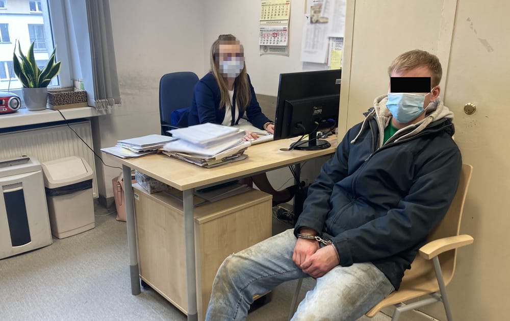 Skuty kajdankami podejrzany siedzi w pokoju przesłuchań na komisariacie policji w towarzystwie policjantki.