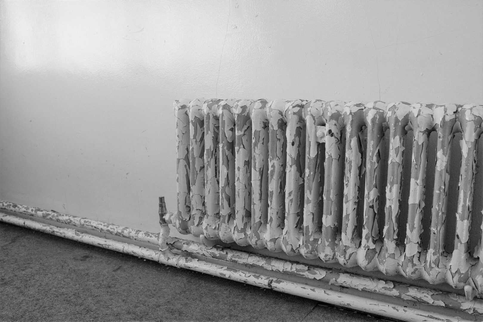 Stary, łuszczący się grzejnik ze starymi rurami.