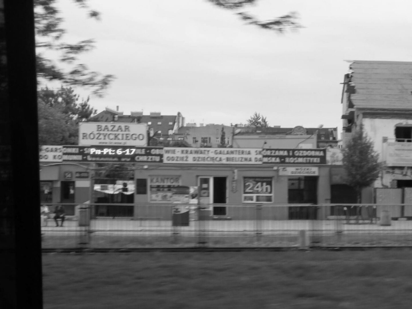 Czarno-białe zdjęcie przedstawiające polską ulicę, na której widać Bazar Różyckiego i sklepy.