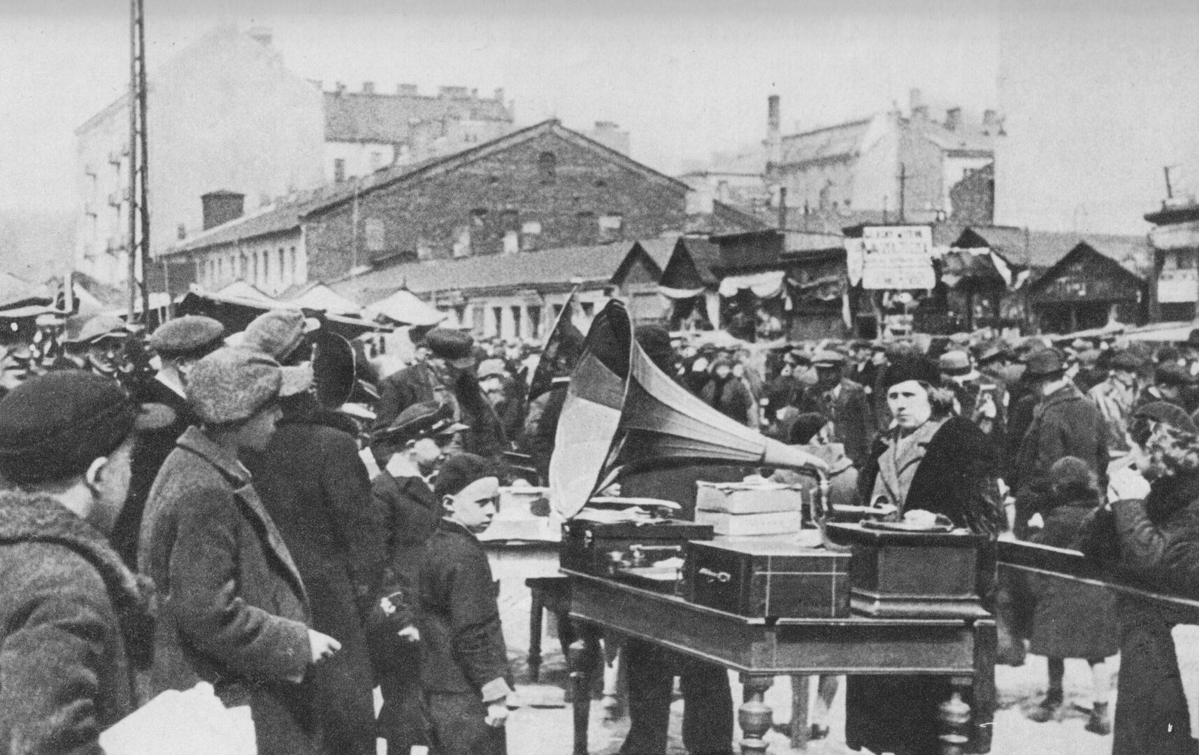 Scena uliczna z lat dwudziestych XX wieku: dźwięki gramofonu dla licznego tłumu na targu pod gołym niebem.