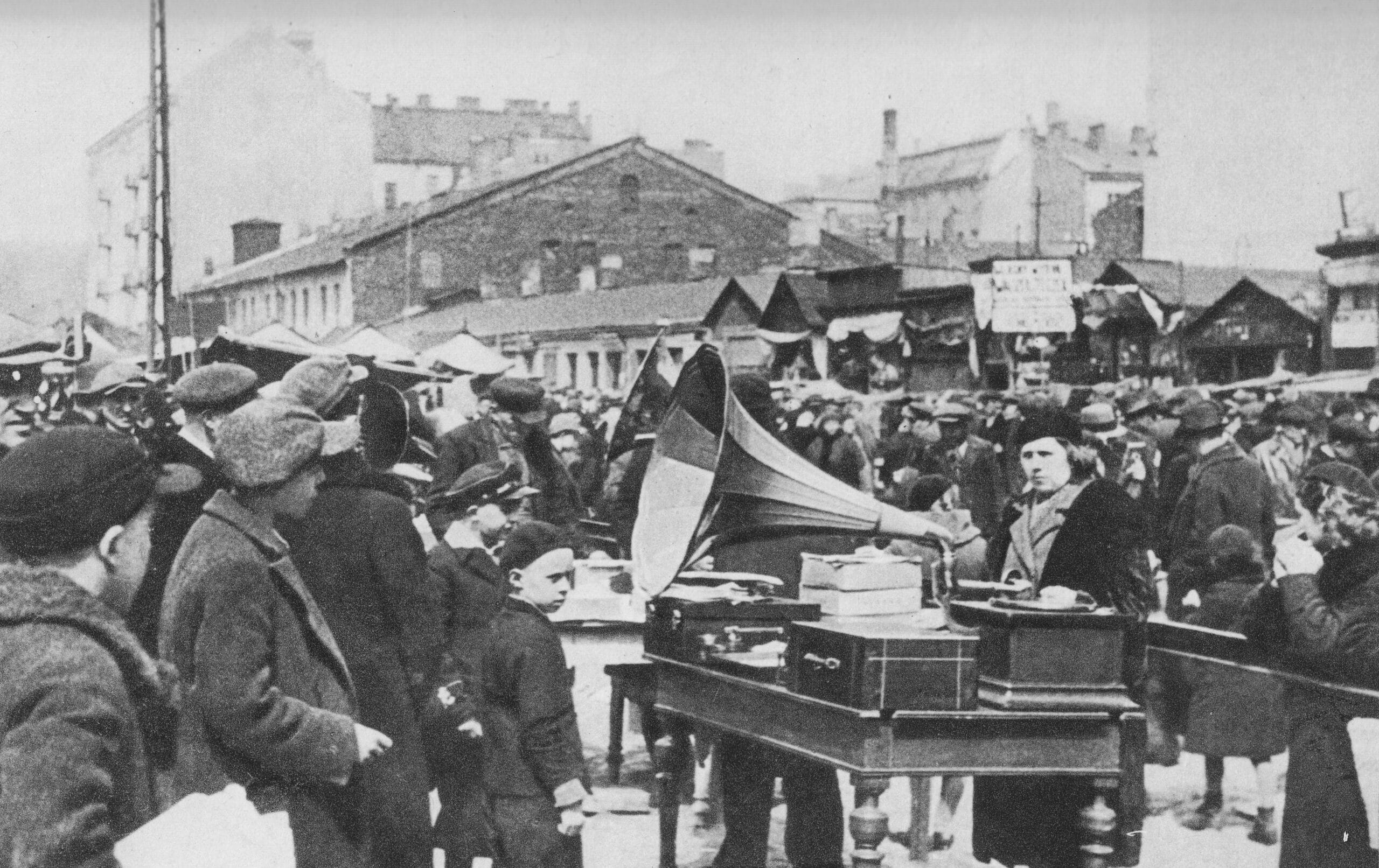 Scena uliczna z lat dwudziestych XX wieku: dźwięki gramofonu dla licznego tłumu na targu pod gołym niebem.