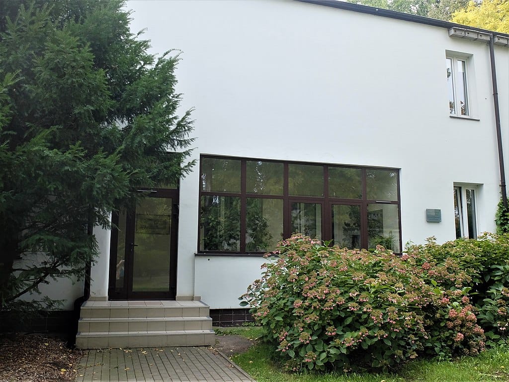 Nowoczesny biały budynek z dużymi oknami i krzewami