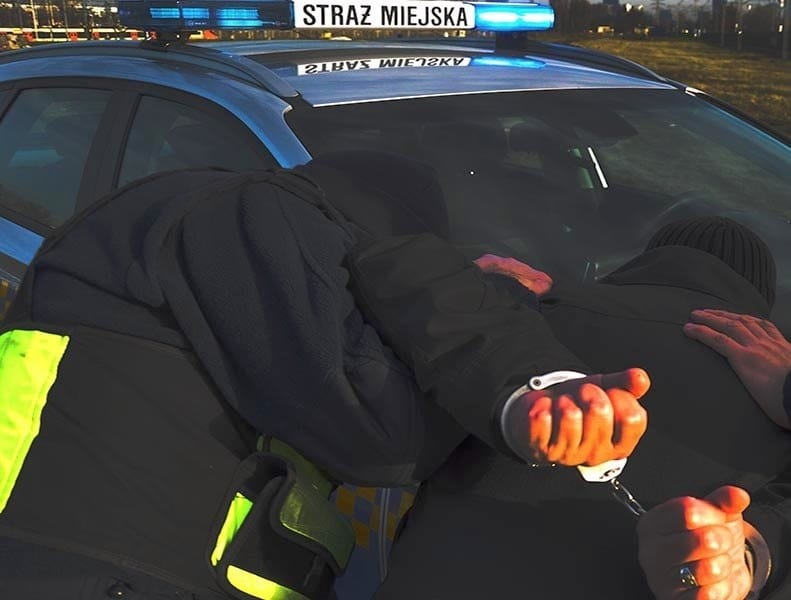 Policjanci zatrzymujący podejrzanego, widoczne kajdanki. "Straż Miejska" w radiowozie.
