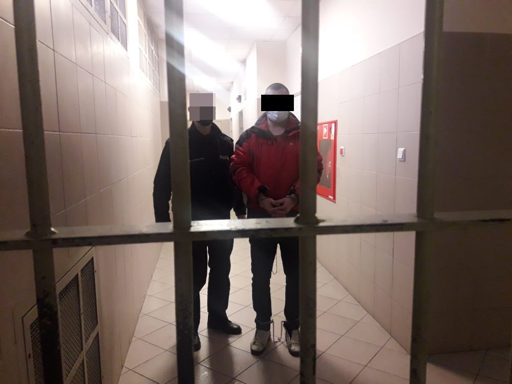 Skuty podejrzany eskortowany przez policjanta korytarzem więziennym.