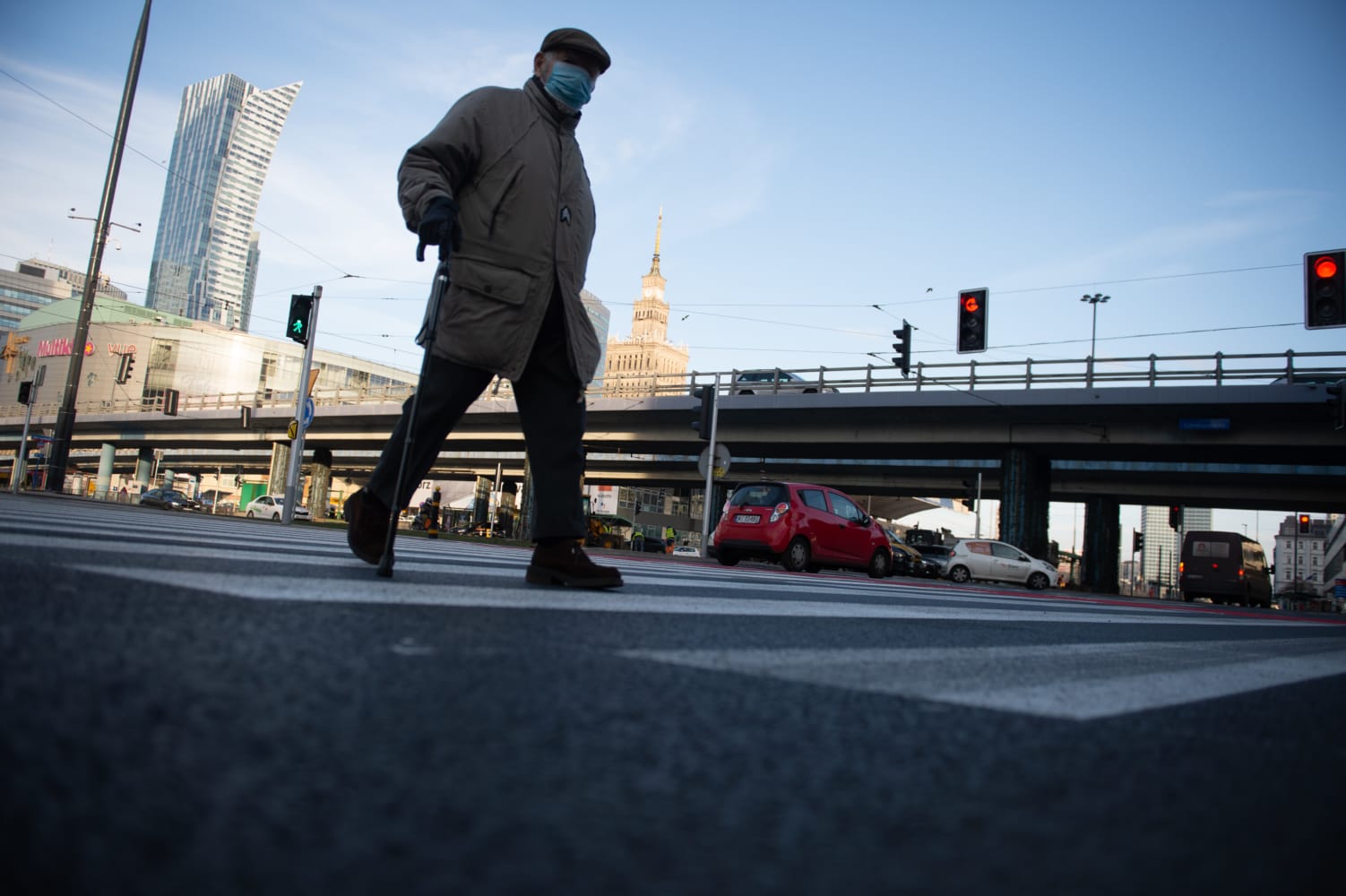 Starszy mężczyzna z laską przechodzi przez ulicę miasta w masce na twarzy