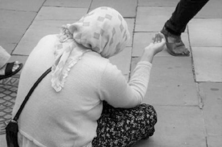 Kobieta w chuście na głowie żebrze na ulicy miasta.