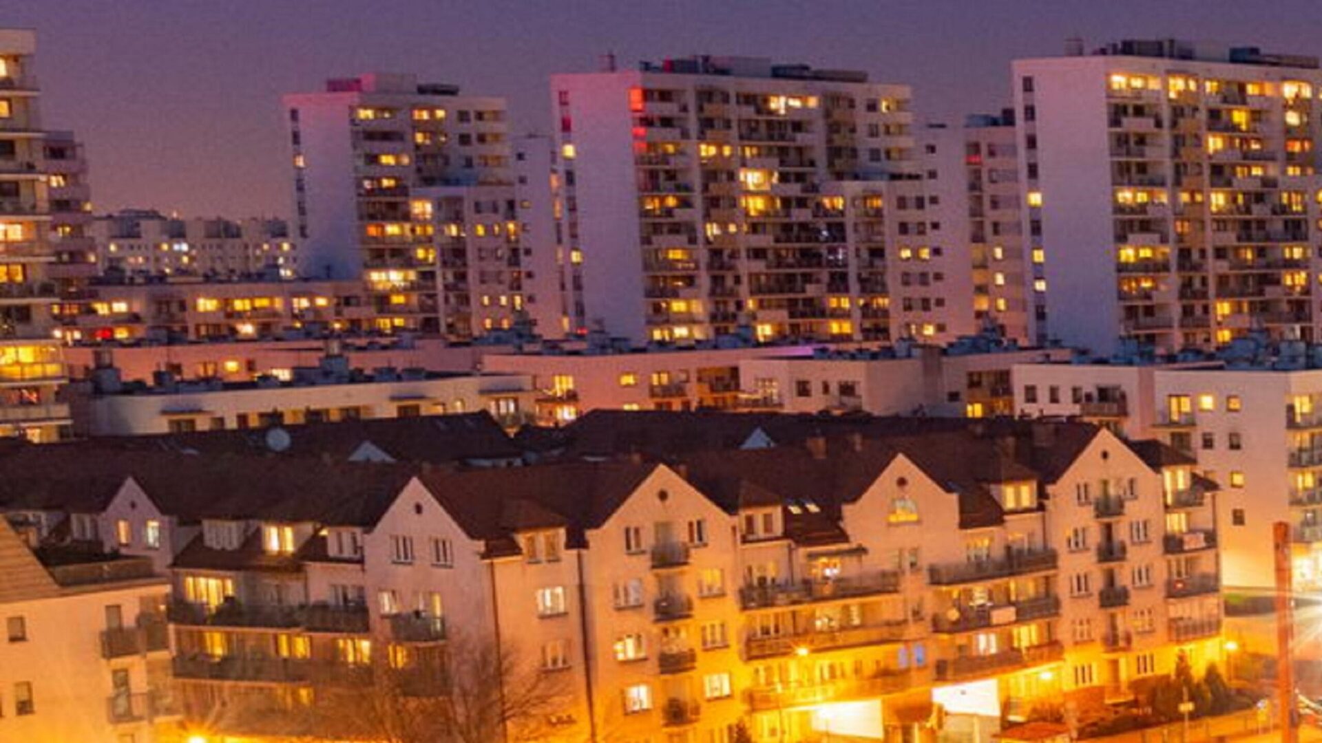 Nocny widok miejskich bloków mieszkalnych z ciepłym oświetleniem wnętrz.