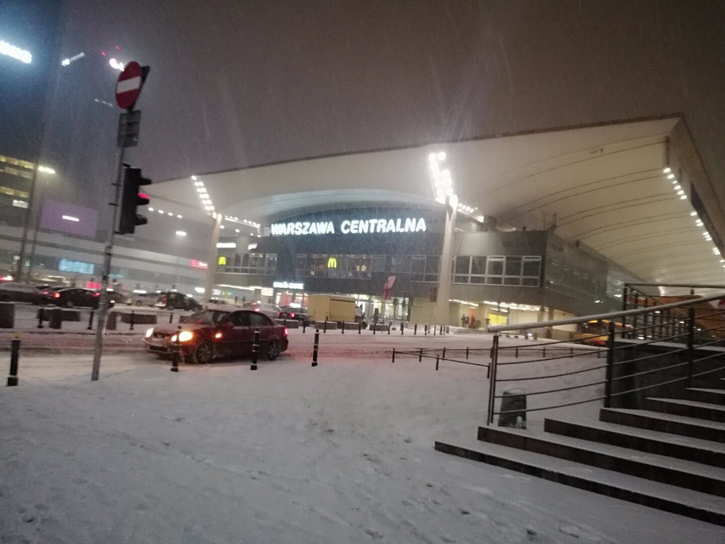 Dworzec Centralny w Warszawie pokryty śniegiem w nocy. Widoczny znak "Warszawa Centralna".