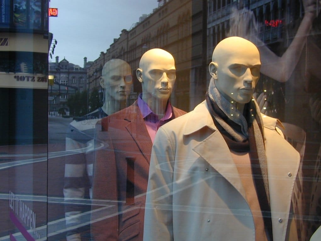 Trzy męskie manekiny na wystawie sklepowej, ubrane w płaszcze i garnitury.