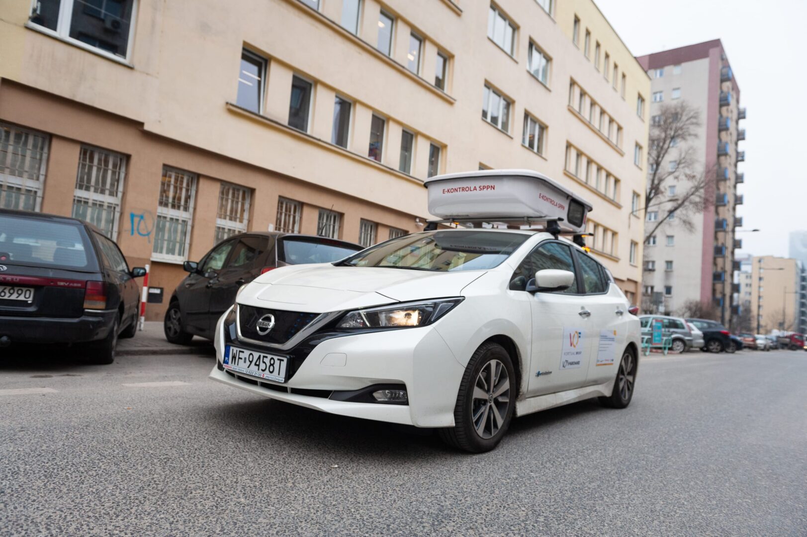Biały samochód elektryczny Nissan Leaf z wyposażeniem dachowym, tablica rejestracyjna WF-9458T.