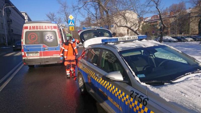 Ratownicy na miejscu wypadku: karetka pogotowia, radiowóz i ratownicy medyczni.