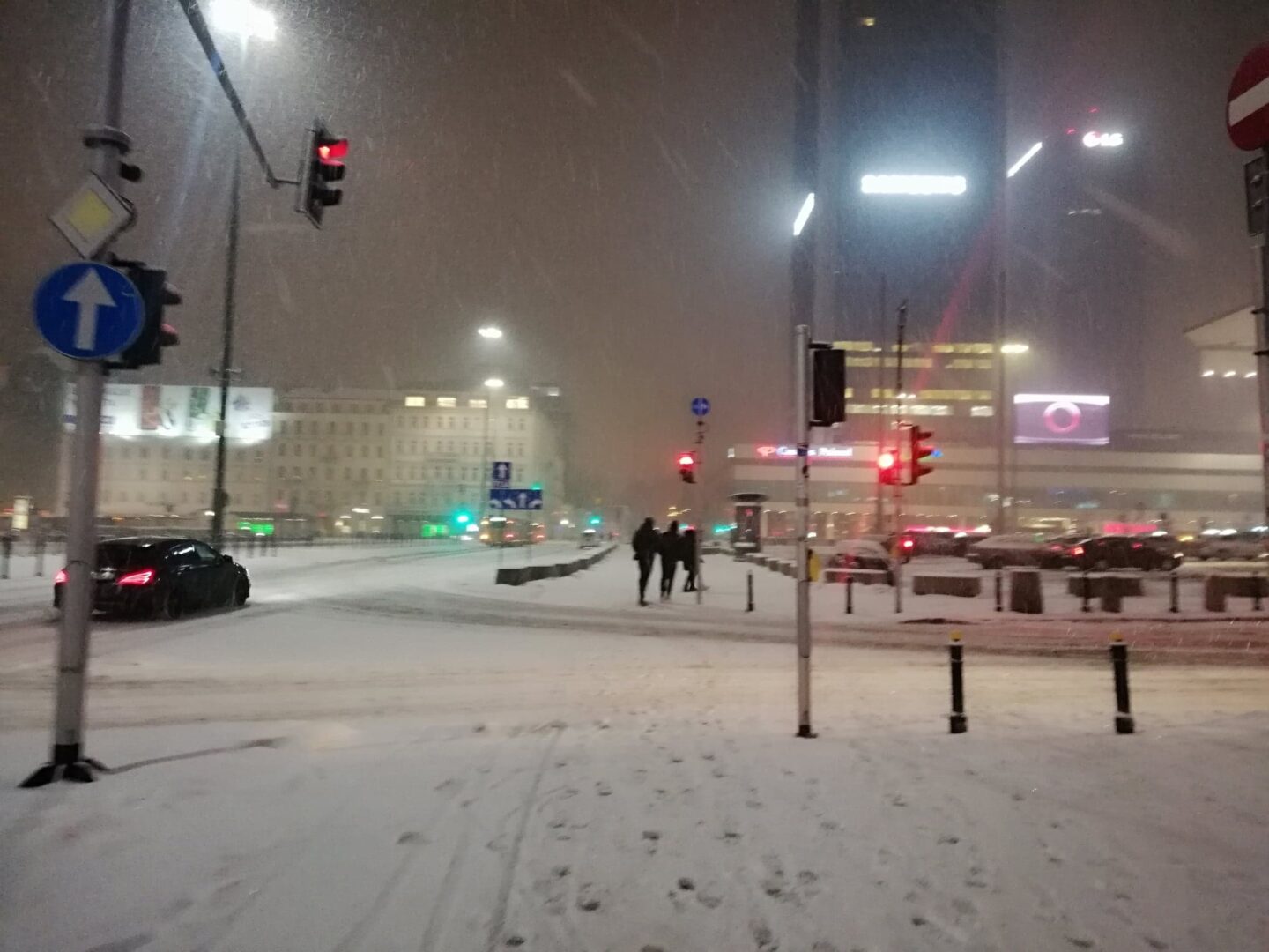 Zaśnieżona ulica miasta nocą, mnóstwo samochodów i pieszych.