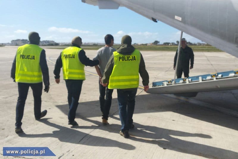 Policjanci z polskiej policji eskortują podejrzanego opuszczającego samolot. Widoczne są kamizelki POLICJI.