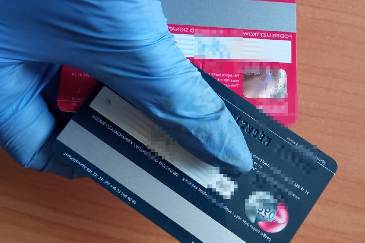 Zbliżenie dłoni w rękawiczkach trzymających dwie karty bankowe: jedną czerwoną i jedną czarną.