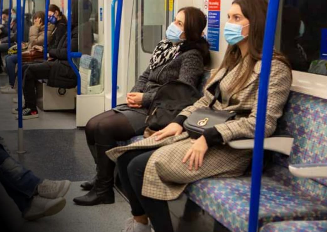 Pasażerowie noszący maseczki ochronne w zatłoczonym metrze londyńskim w czasie pandemii COVID-19.