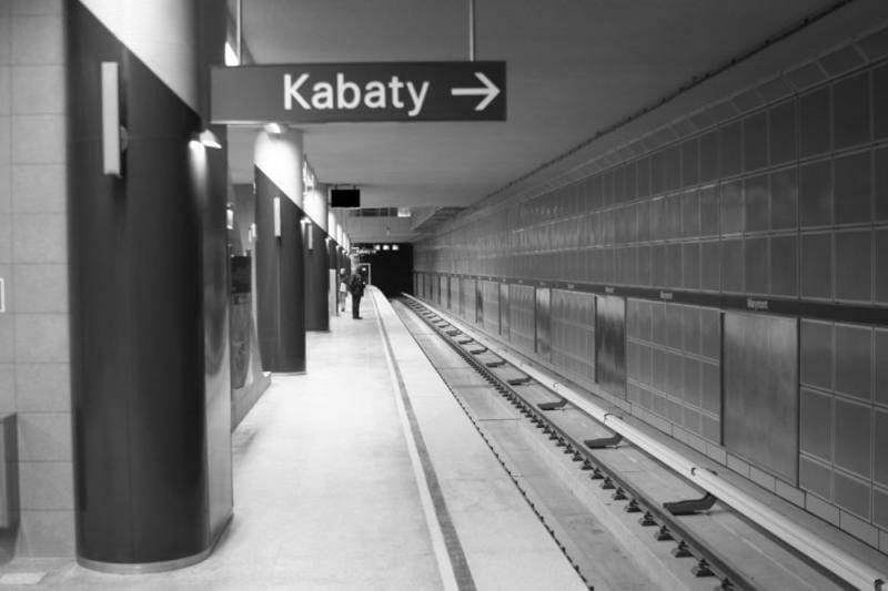 Peron stacji metra warszawskiego, widoczny napis "Kabaty". Pusty peron z torami.