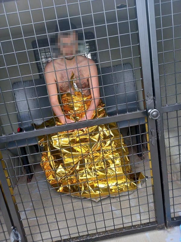 Mężczyzna owinięty w złoty koc ratunkowy siedzi w klatce pojazdu.