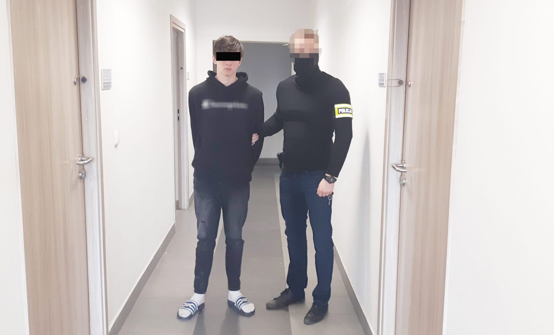 Policjant eskortujący zatrzymanego młodego mężczyznę korytarzem.