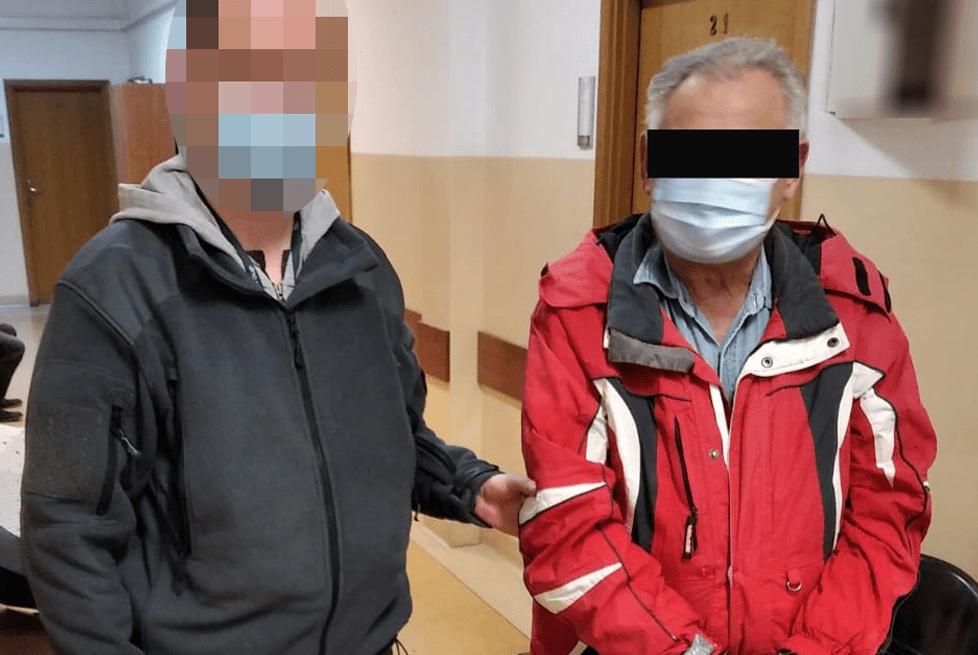 Dwóch mężczyzn w kurtkach, jeden w areszcie, twarze częściowo zasłonięte.