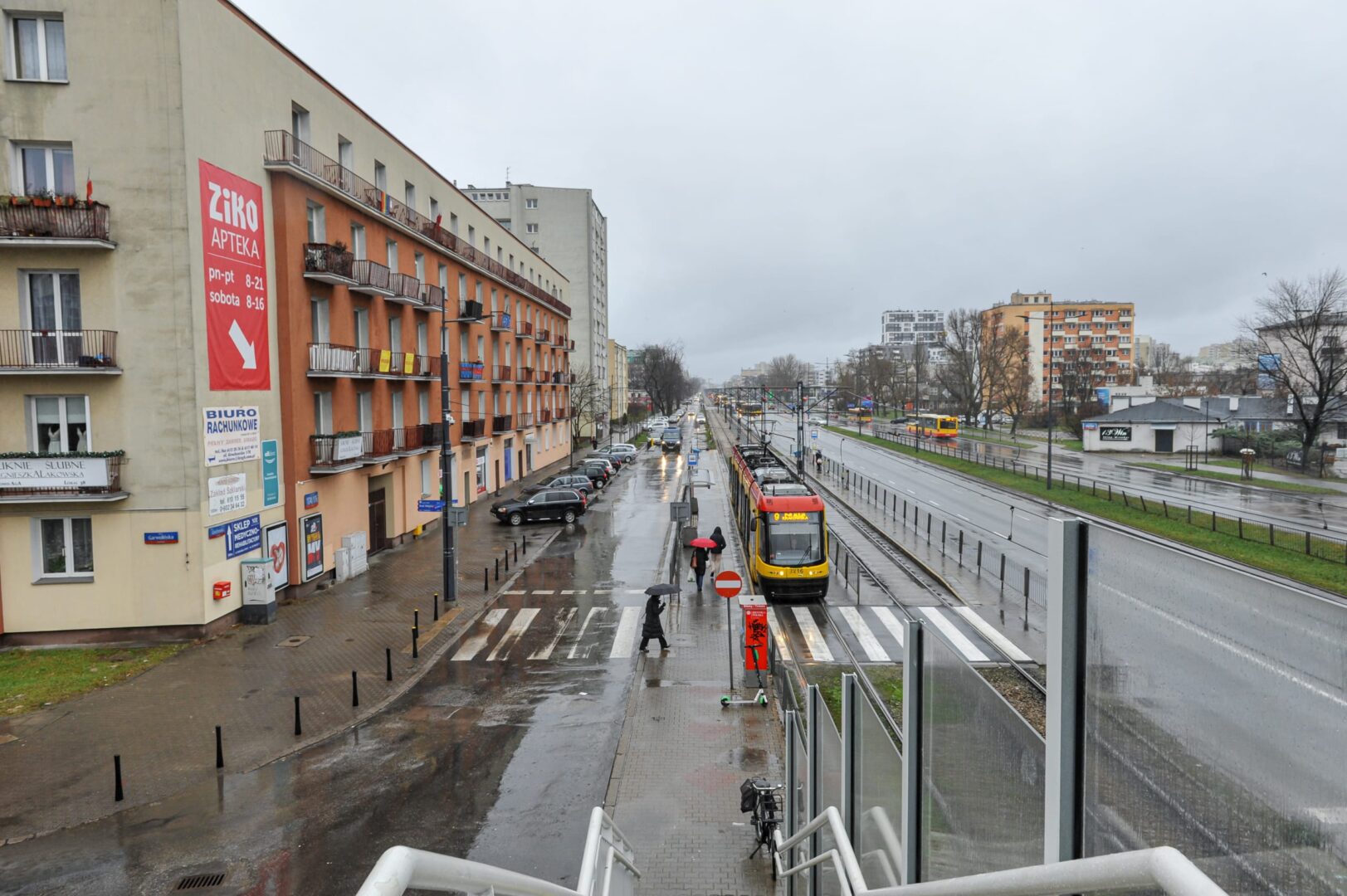 Deszczowy dzień w Warszawie: tramwaj na ulicy miejskiej, wśród pieszych i budynków.