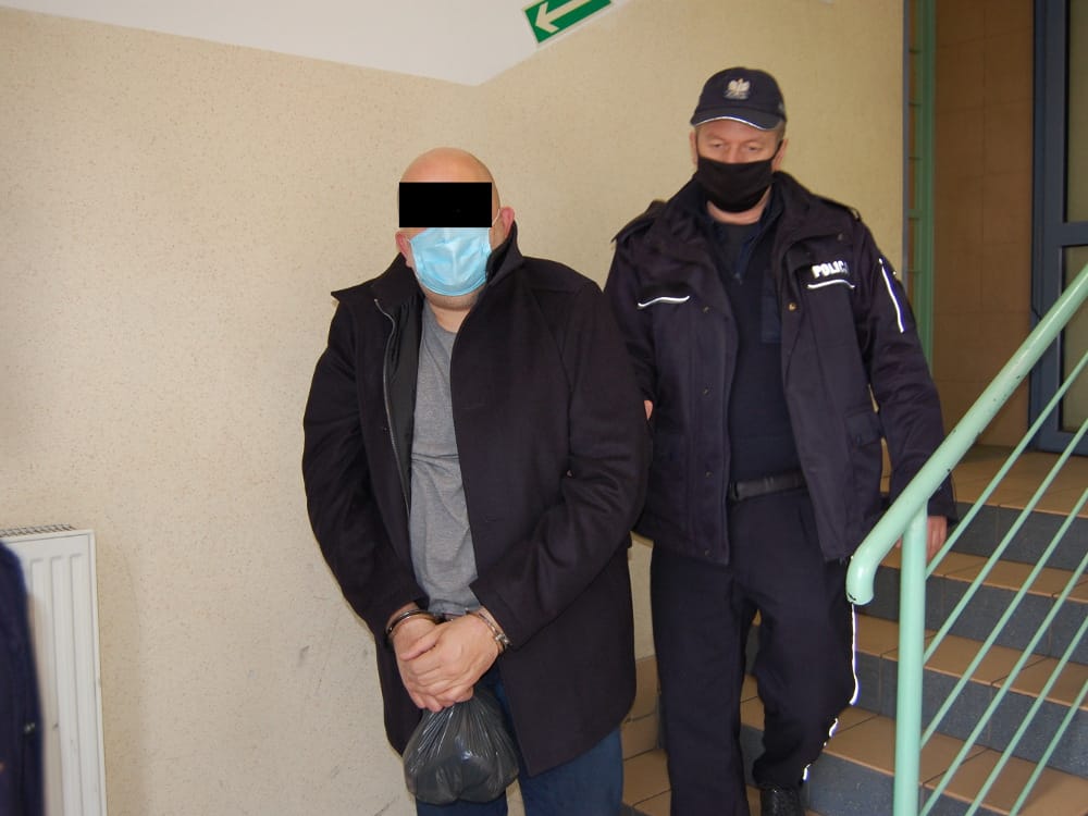 Policja eskortuje podejrzanego w kajdankach po schodach