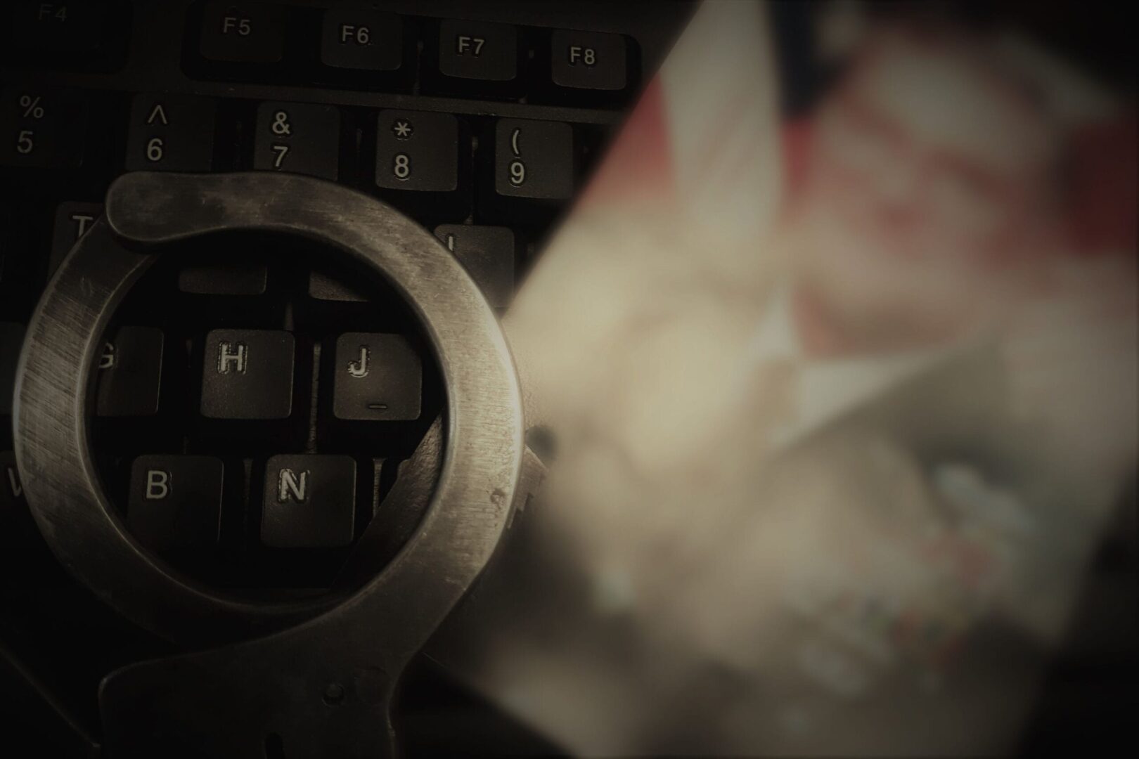 Kajdanki na klawiaturze obok rozmazanego zdjęcia; śledztwo w sprawie cyberprzestępczości.