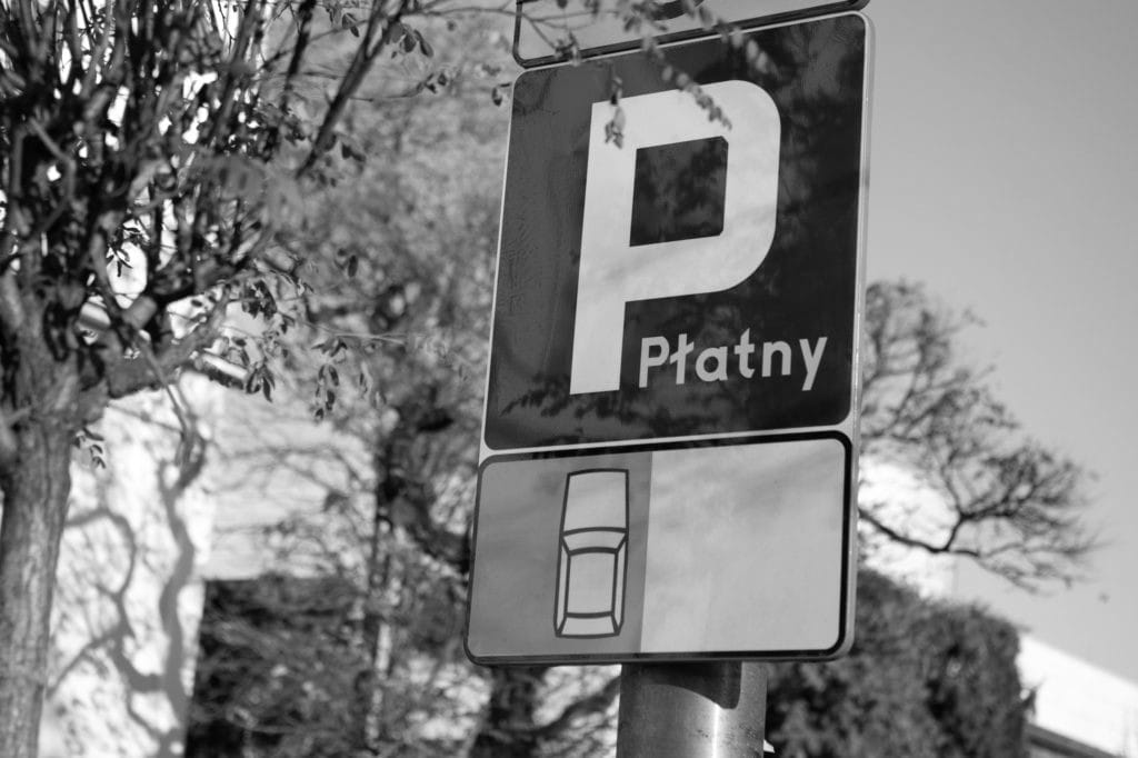 Znak informujący o płatnym parkingu, czarno-biały, z literą „P” i napisem „Płatny”.
