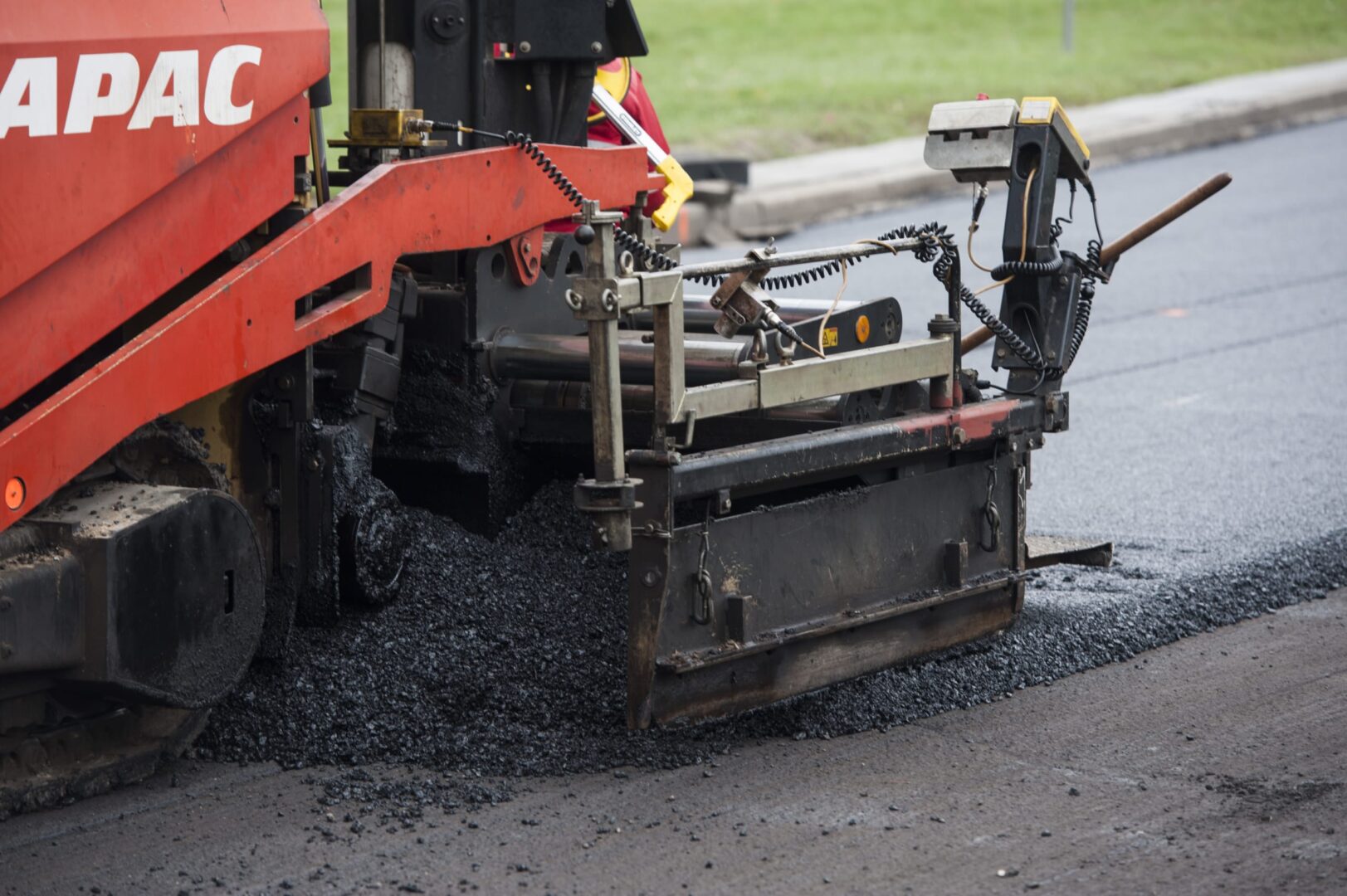 Układarka asfaltu układająca świeży asfalt podczas budowy drogi. Widoczne jest logo APAC.