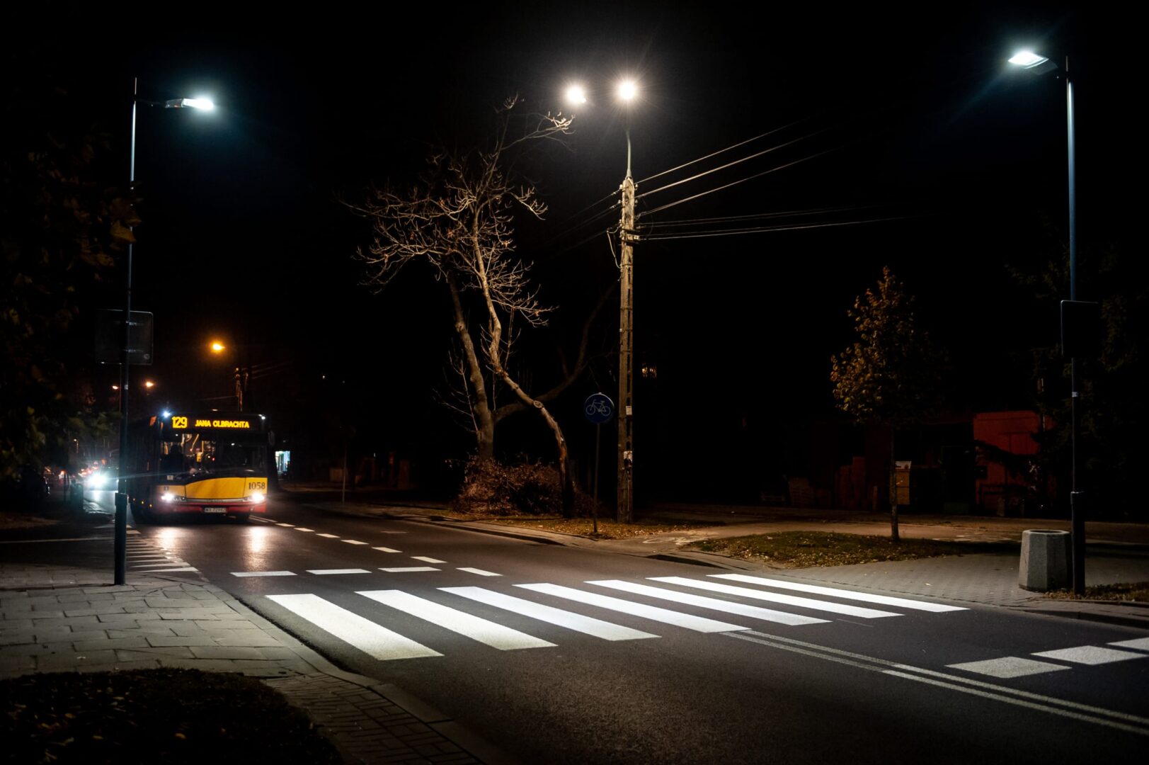Nocny widok ulicy z autobusem linii 1058 na trasie Jana Olbrachta i przejściem dla pieszych.