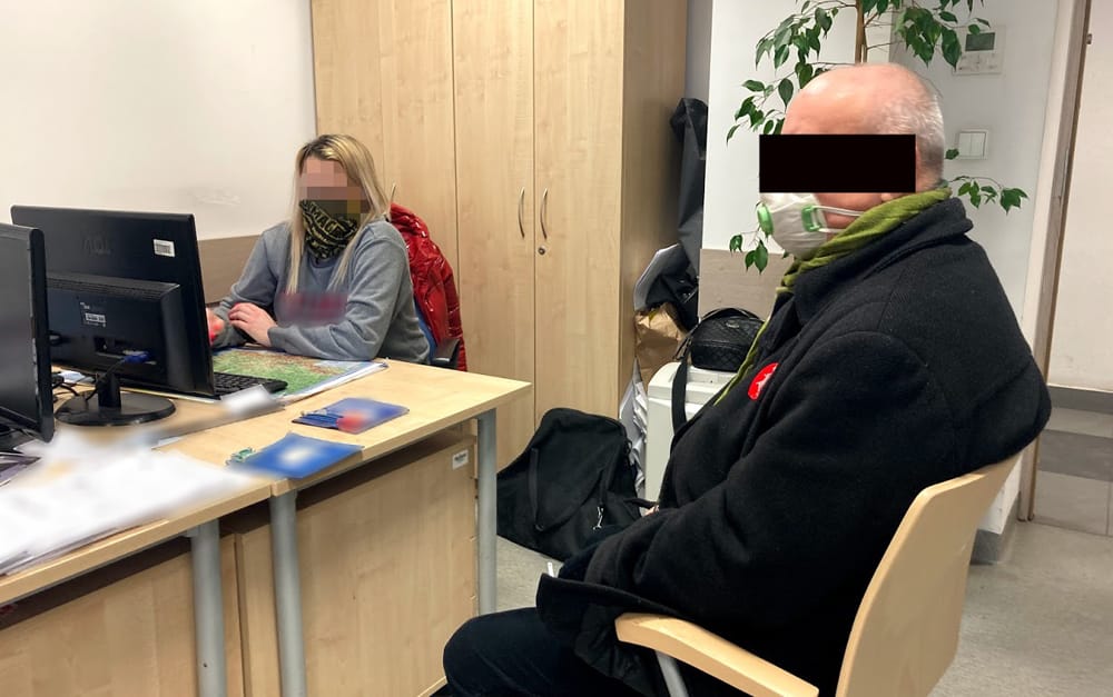 Dwie osoby siedzą przy biurku w biurze, jedna pracuje na komputerze.