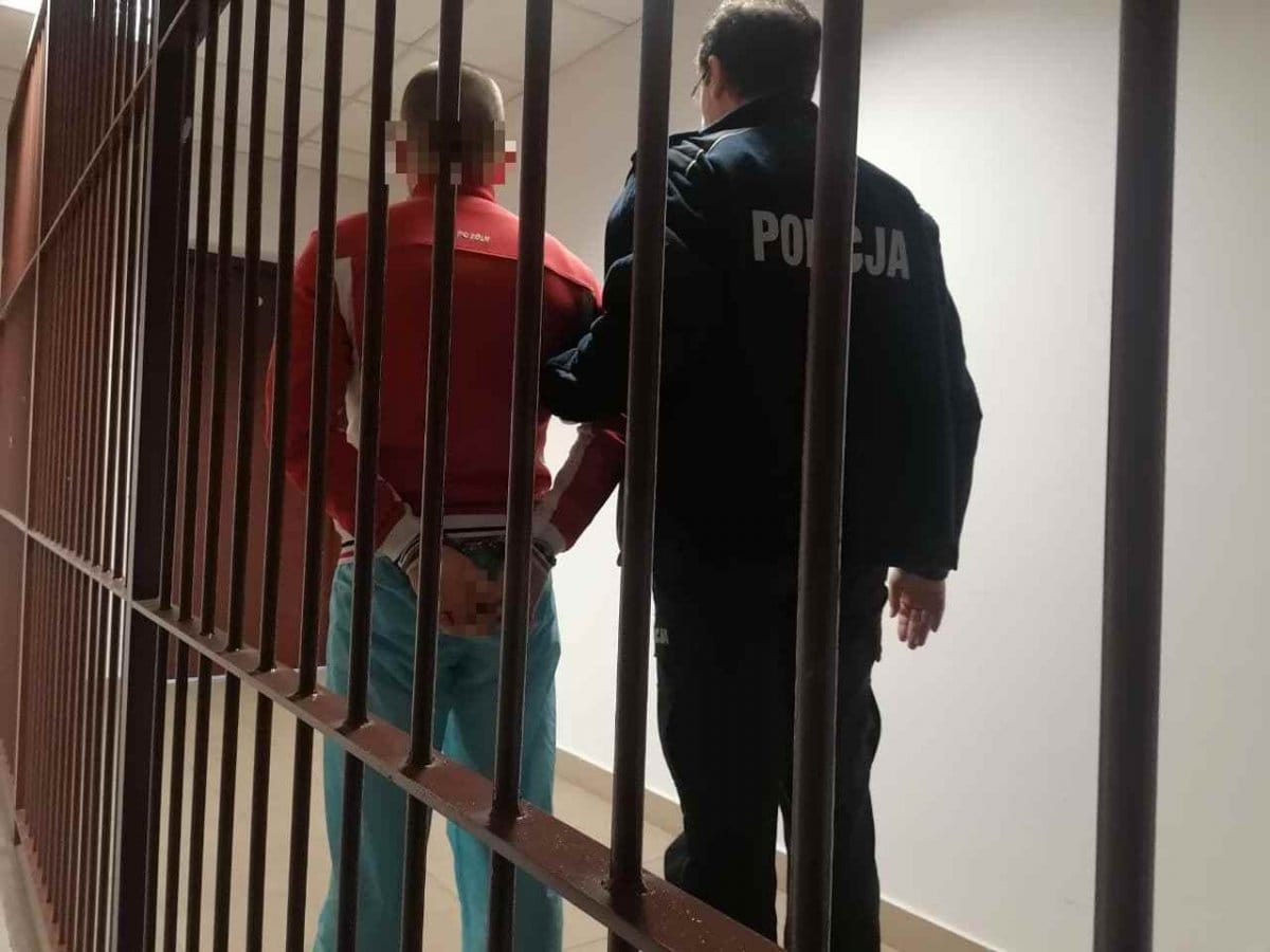 Policjant eskortujący podejrzanego w kajdankach do aresztu.