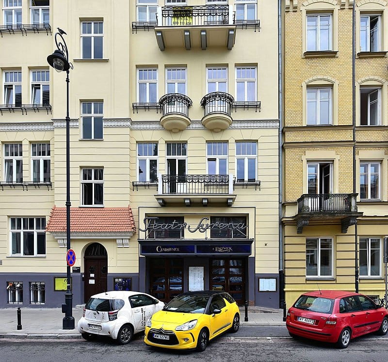 Teatr Syrena w Warszawie, historyczny teatr, znajduje się między dwoma budynkami. Samochody zaparkowane przed nim.