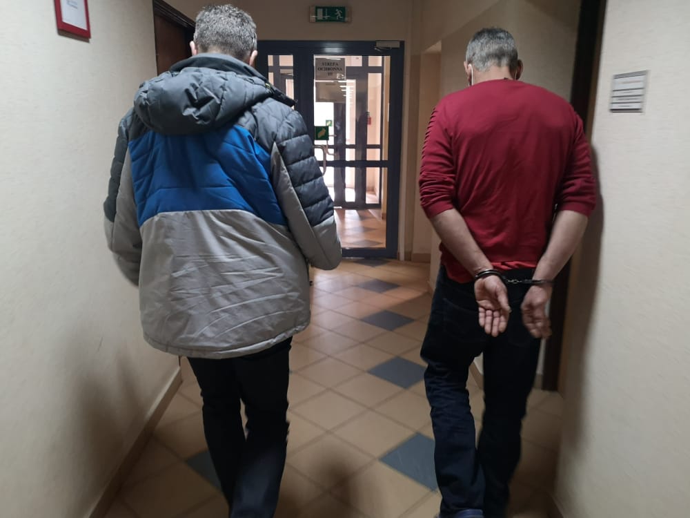 Dwóch mężczyzn w kajdankach idących korytarzem.