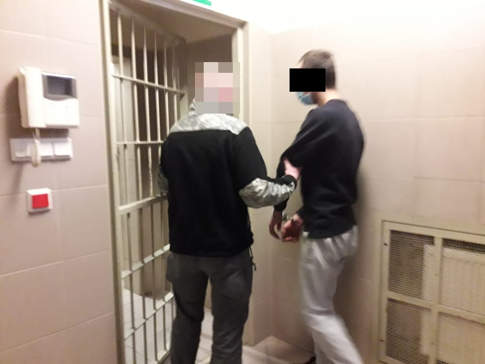 Policjant eskortujący podejrzanego w kajdankach do celi więziennej.