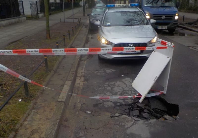 Naprawa dziury w miejskiej ulicy zablokowanej przez radiowozy i taśmę ostrzegawczą.