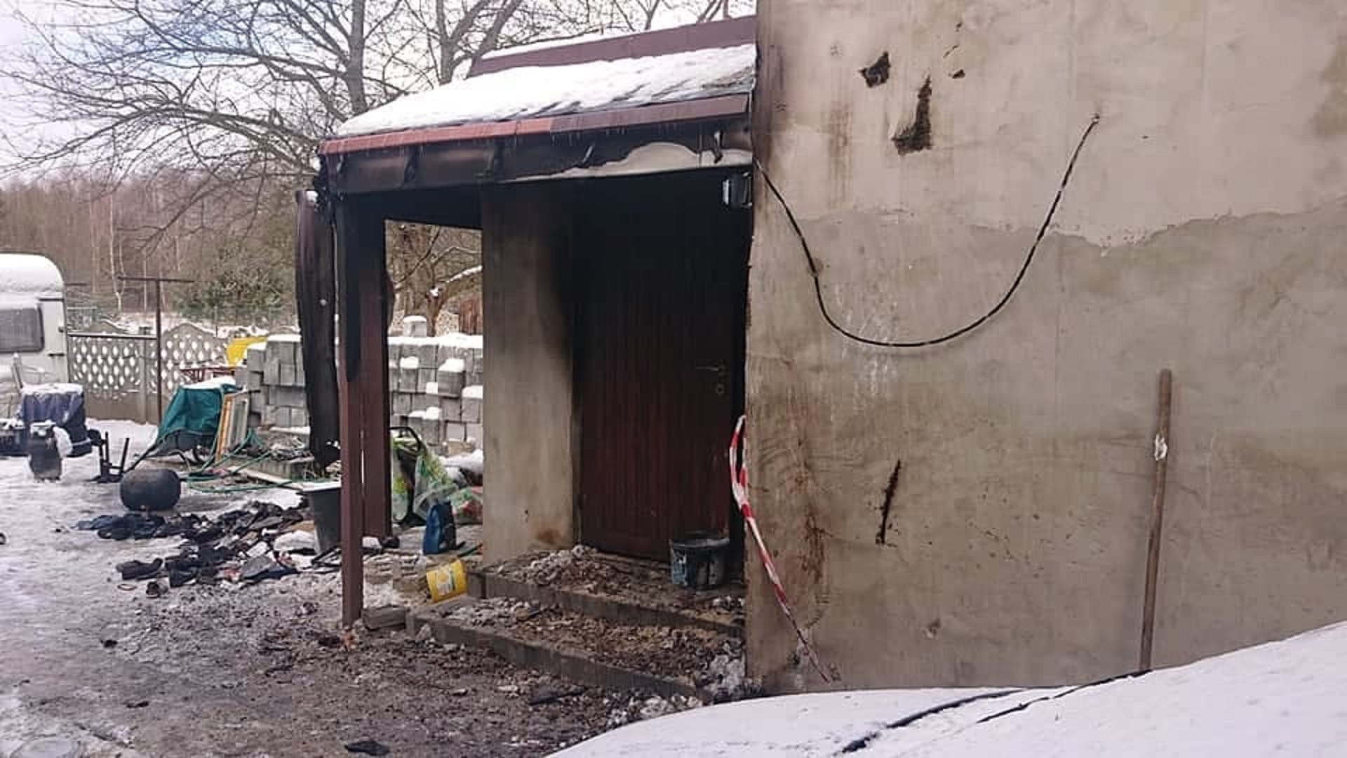 Skutki pożaru małego budynku, widoczne uszkodzenia konstrukcji i gruz na ziemi.