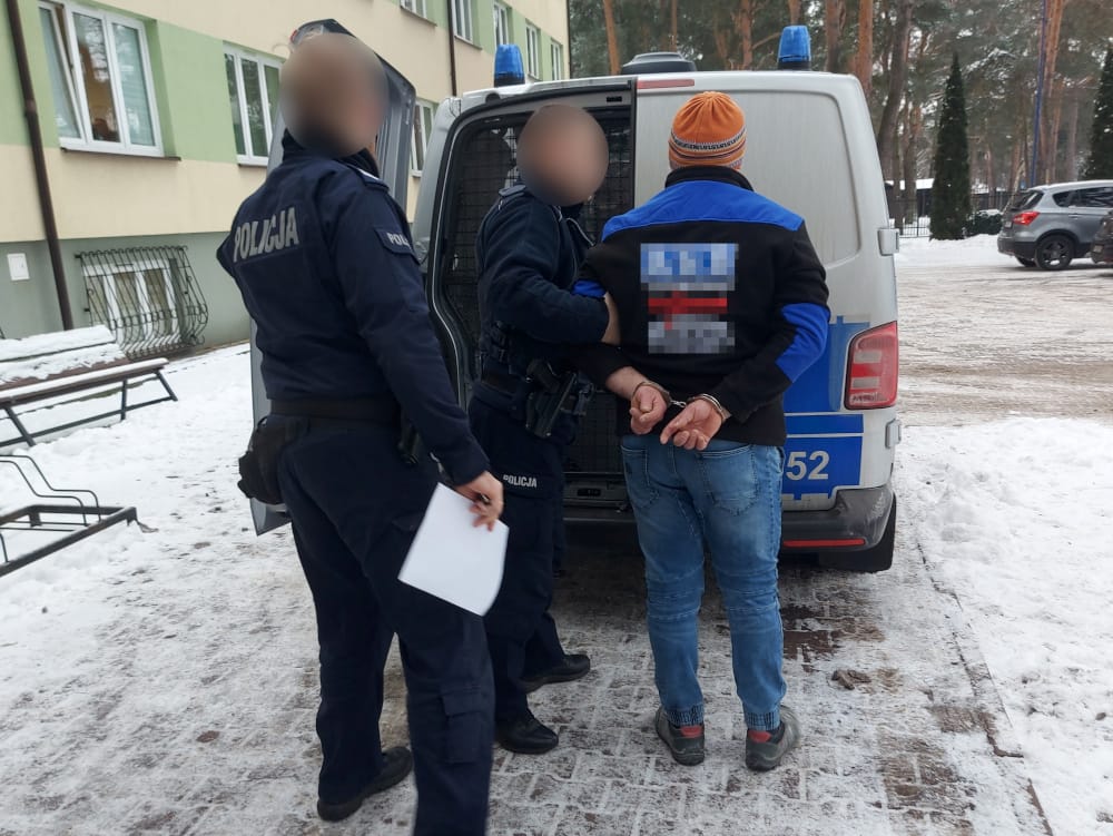 Policjanci zatrzymują podejrzanego w kajdankach w pobliżu radiowozu.