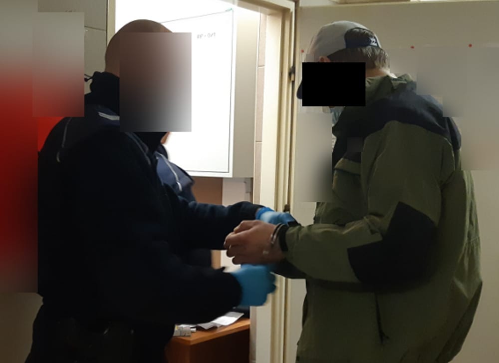 Policjant aresztujący podejrzanego z kajdankami na rękach.