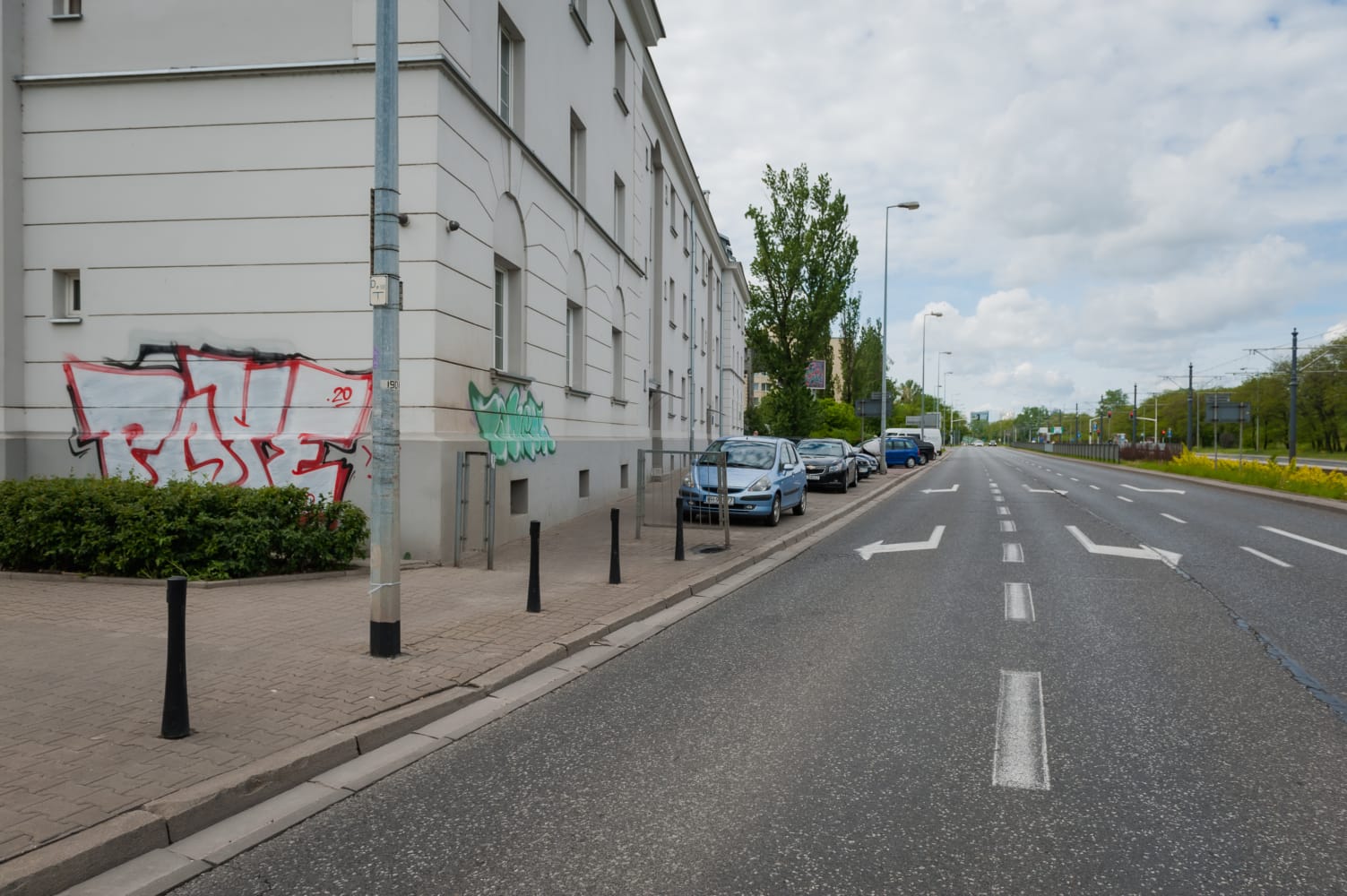 Samochody zaparkowane wzdłuż miejskiej ulicy z graffiti na budynku.
