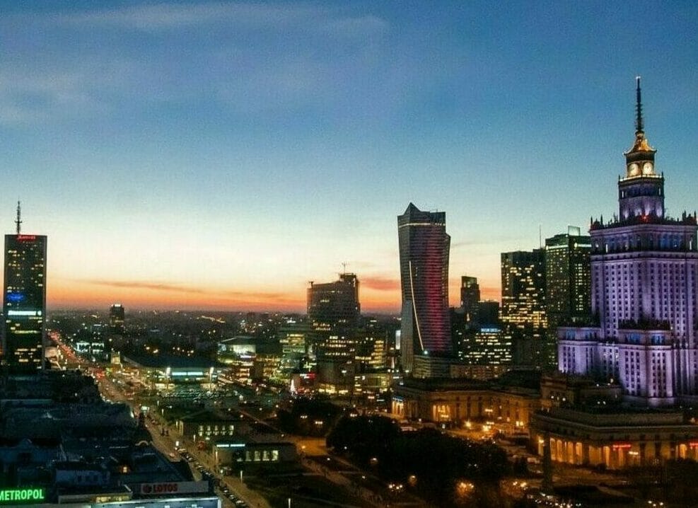 Widok na Warszawę o zachodzie słońca, z Pałacem Kultury i Nauki oraz nowoczesnymi wieżowcami.
