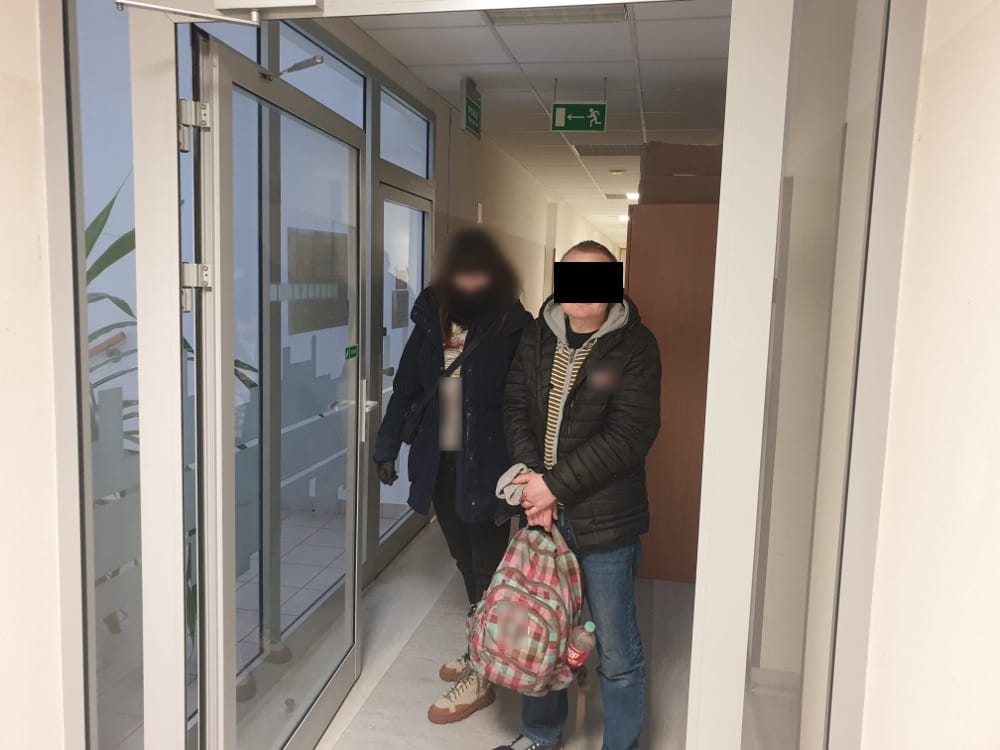 Dwie osoby stoją na korytarzu, jedna z nich niesie plecak.