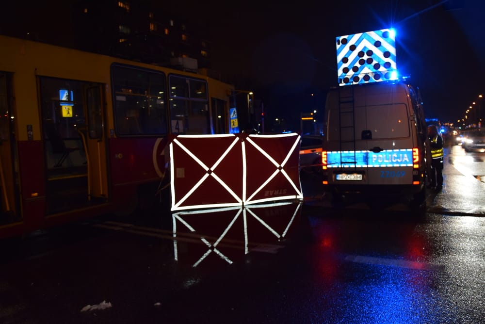 Nocny wypadek drogowy z udziałem radiowozu i tramwaju, droga zamknięta odblaskową barierą.