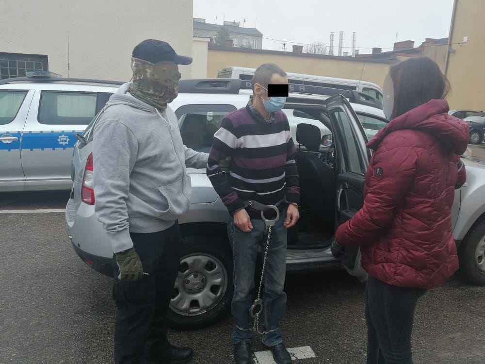 Policjanci zatrzymują podejrzanego w kajdankach w pobliżu samochodu