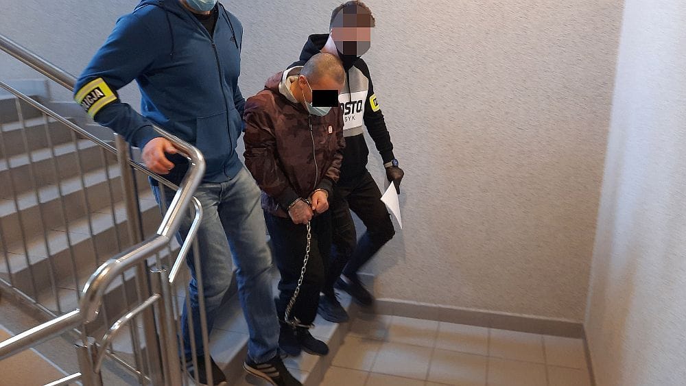 Policja eskortuje podejrzanego w kajdankach po schodach