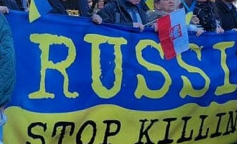 Protestujący trzymają transparent z napisem „Rosja, przestań zabijać” w barwach ukraińskich.