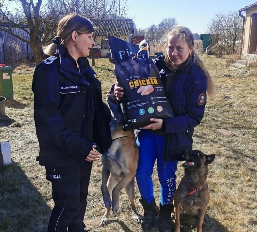 Dwie kobiety przekazują karmę dla psów o imieniu Piper psom rasy belgijski malinois.