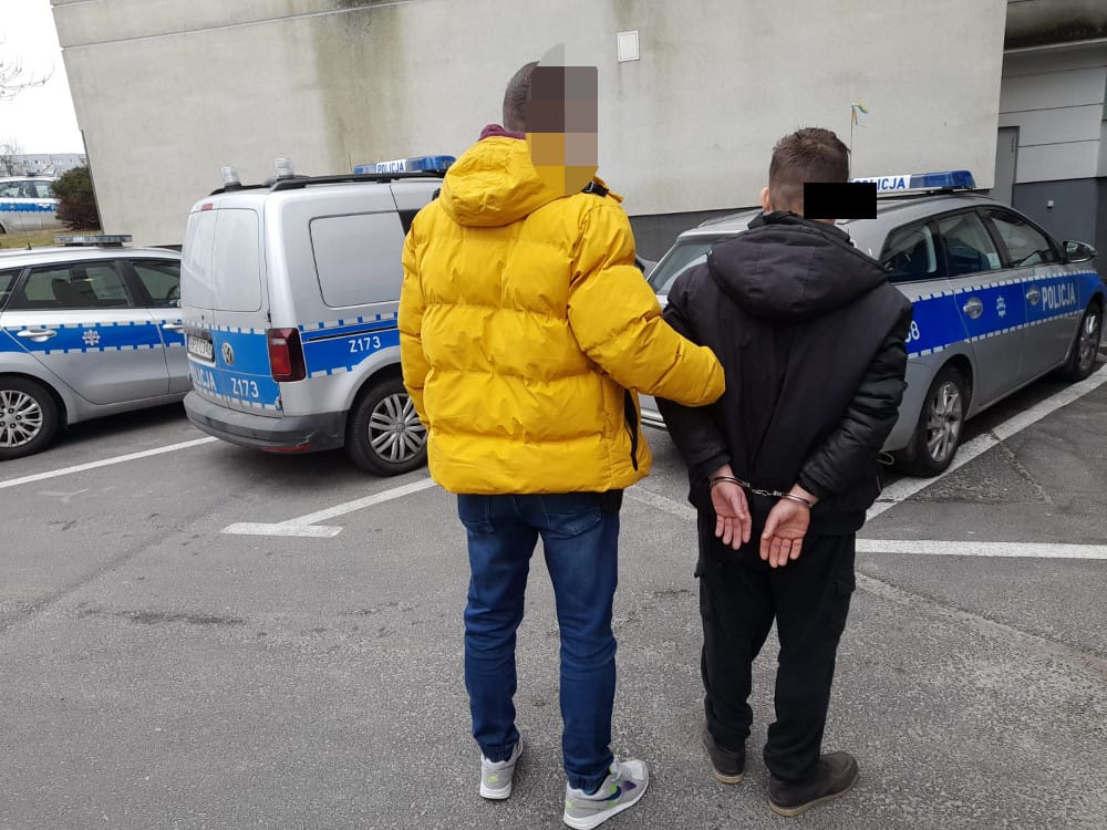 Policjanci zatrzymują podejrzanego w kajdankach.