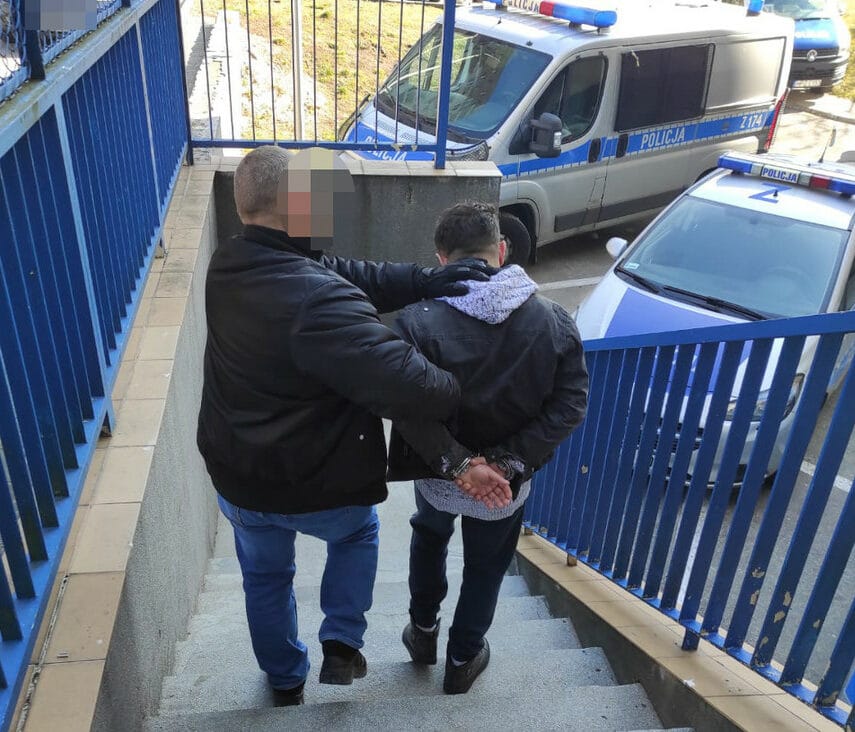 Dwóch policjantów eskortuje skutego podejrzanego po schodach.